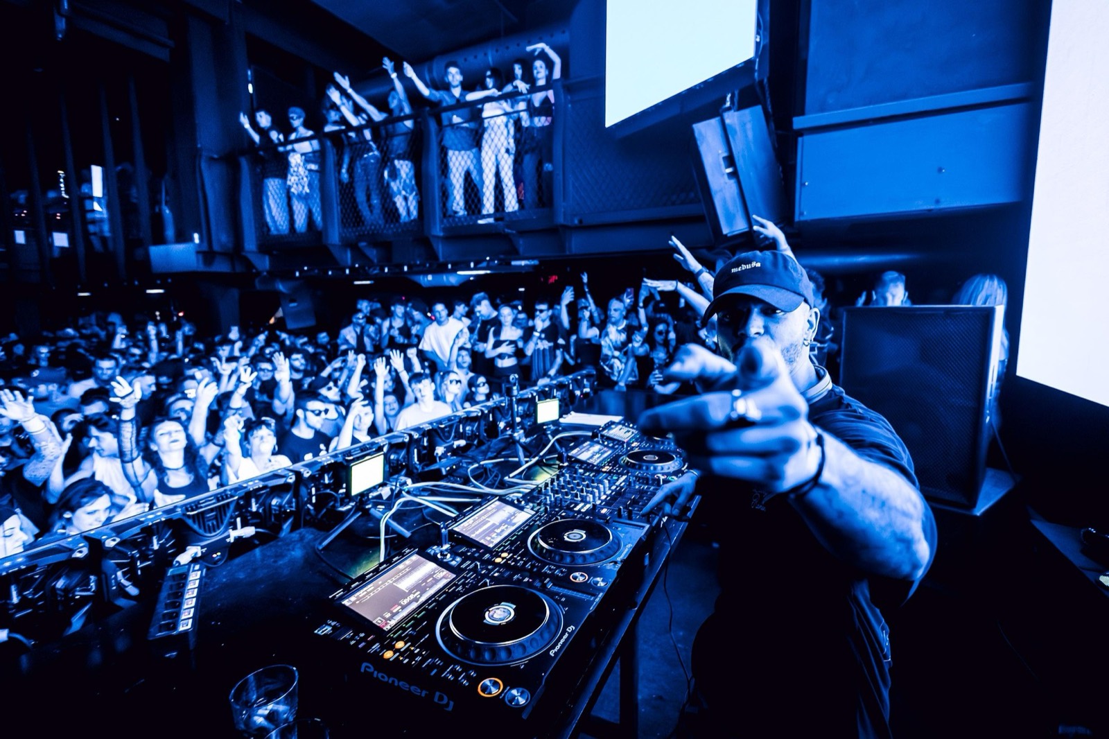 DJ zeigt vom Pult aus auf das Publikum
